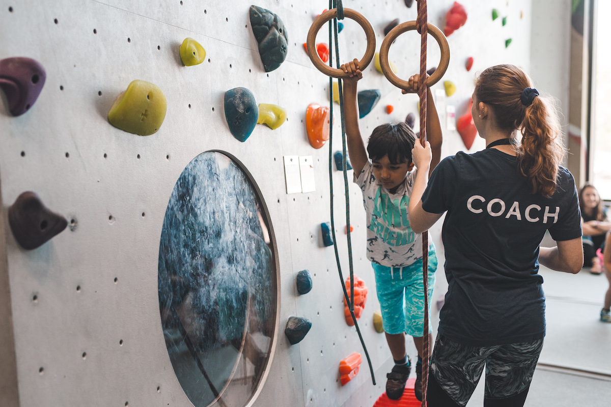 camp coach overlooking young boy on gymnast rings