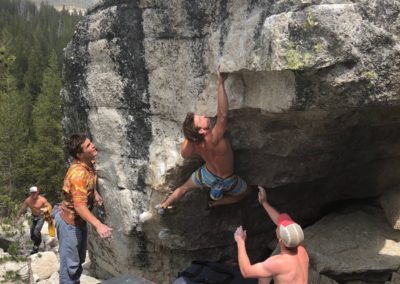 man climbing boulder outdoors while two other men spot